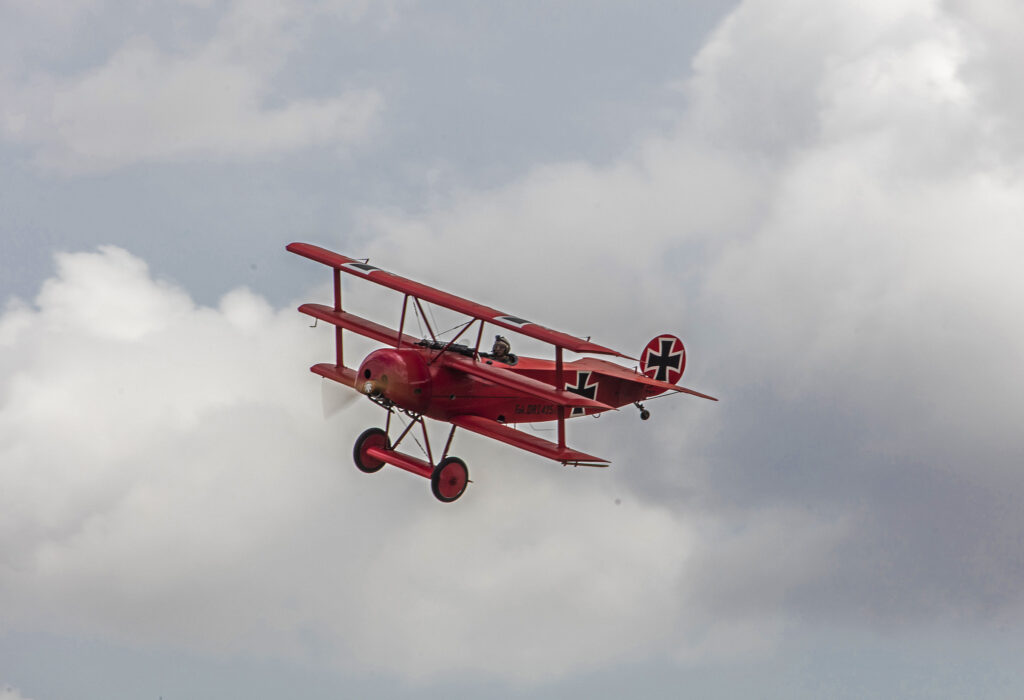 All-red Fokker Dr.I triplane, stencilled Fok. DrI 425/17, banking against towering cloud.