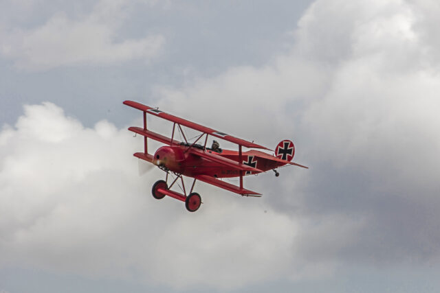 All-red Fokker Dr.I triplane, stencilled Fok. DrI 425/17, banking against towering cloud.